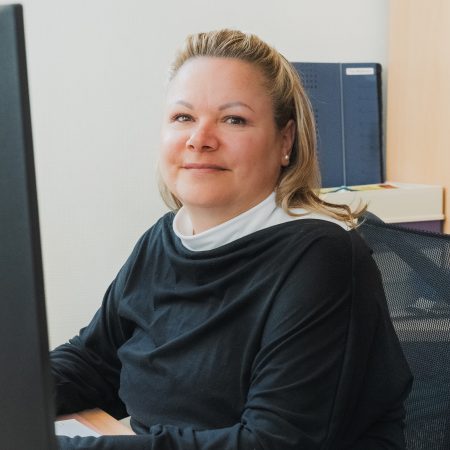 Eine Mitarbeiterin der Benke Steuerberatung sitzt an ihrem Arbeitsplatz vor dem Computer und blickt freundlich in die Kamera.