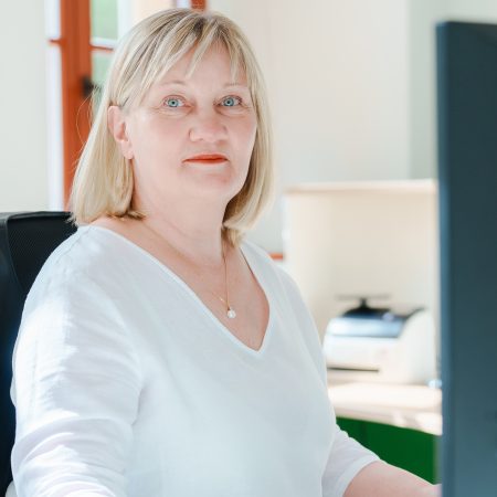 Eine Mitarbeiterin der Benke Steuerberatung sitzt an ihrem Arbeitsplatz und blickt freundlich in die Kamera.