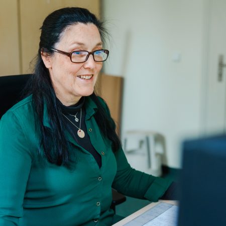 Eine Mitarbeiterin der Benke Steuerberatung sitzt am Schreibtisch, arbeitet am Computer und lächelt dabei freundlich.