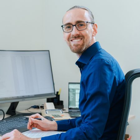 Ein Mitarbeiter der Benke Steuerberatung sitzt am Computer, arbeitet mit Unterlagen und lächelt in die Kamera.