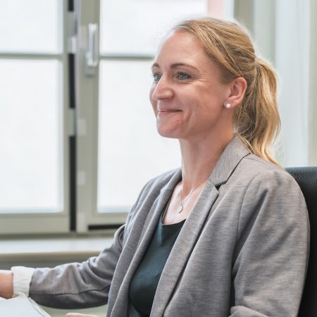 Eine Mitarbeiterin der Benke Steuerberatung sitzt an ihrem Arbeitsplatz und lächelt leicht, während sie zur Seite blickt.