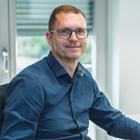 Ein Mitarbeiter der Benke Steuerberatung sitzt an seinem Arbeitsplatz und blickt freundlich in die Kamera.