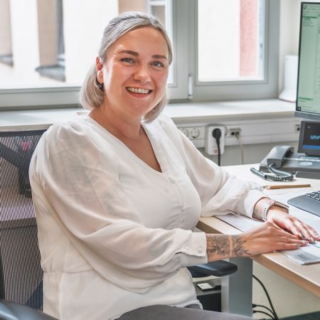 Eine Mitarbeiterin der Benke Steuerberatung sitzt lächelnd am Computerarbeitsplatz und arbeitet in einem hellen Büro.