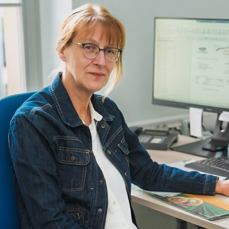 Eine Mitarbeiterin der Benke Steuerberatung sitzt an ihrem Arbeitsplatz vor dem Computer und blickt freundlich in die Kamera.
