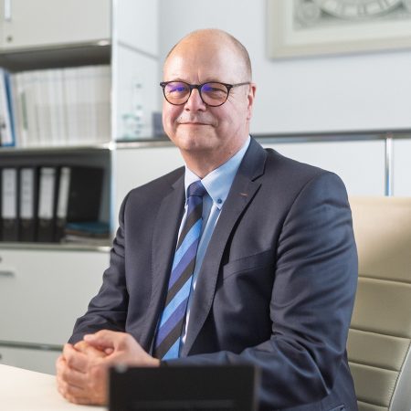 Gründer Ronald Benke sitzt im Büro der Benke Steuerberatung und blickt freundlich in die Kamera.
